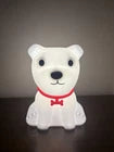 White bear-shaped night light with a red bow tie on a dark surface.