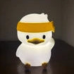 Small white duck plush toy with a yellow headband on a dark background
