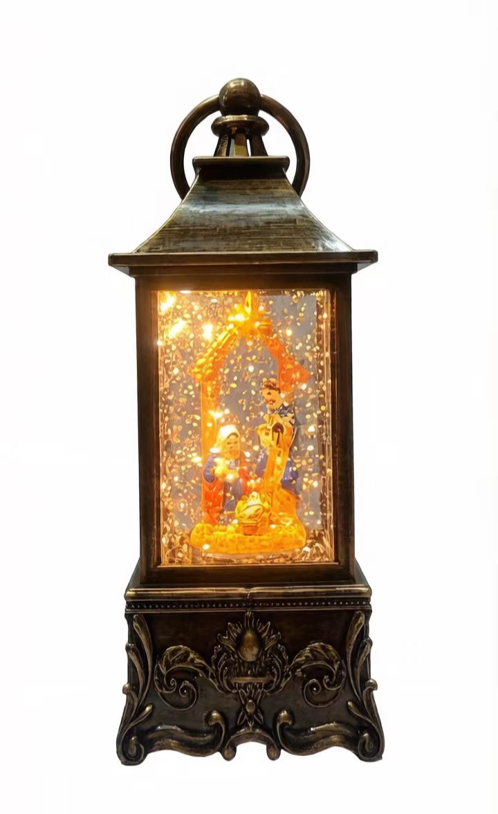 A decorative lantern-style night light with an ornate dark metal frame, glowing warm light, and a nativity scene inside, isolated on a white background.