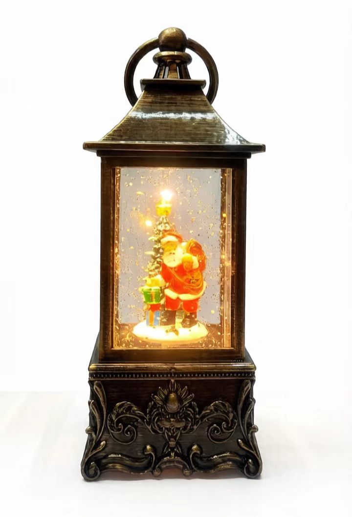 A decorative lantern-shaped Christmas ornament with a dark bronze metal frame, featuring a Santa Claus and tree scene illuminated from within, set against a plain white background.