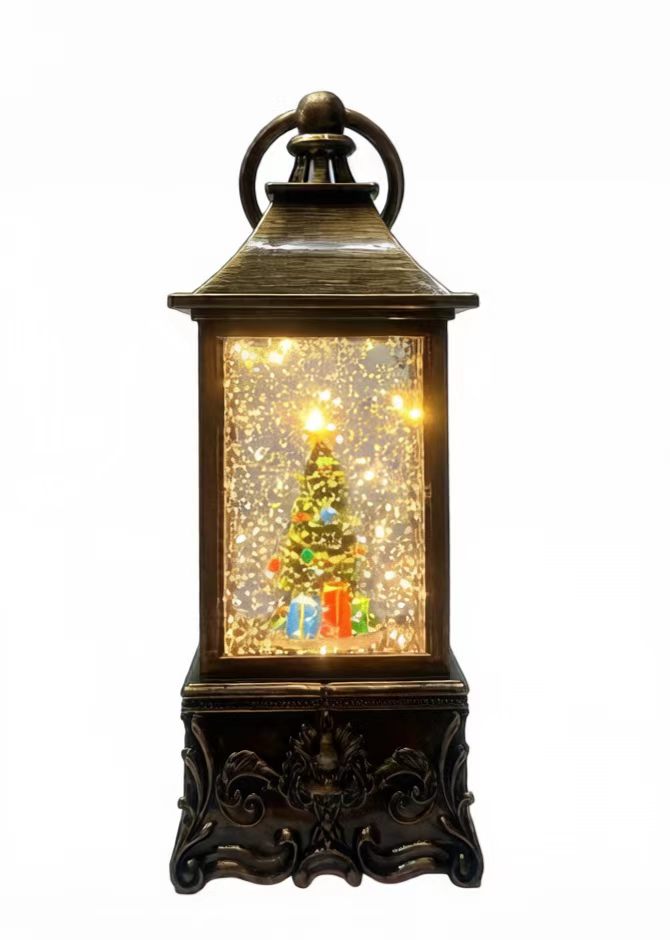A decorative lantern-style Christmas light with a dark bronze metal frame, glowing warm white lights inside, and a small illuminated Christmas tree with colorful gift boxes on a white background.