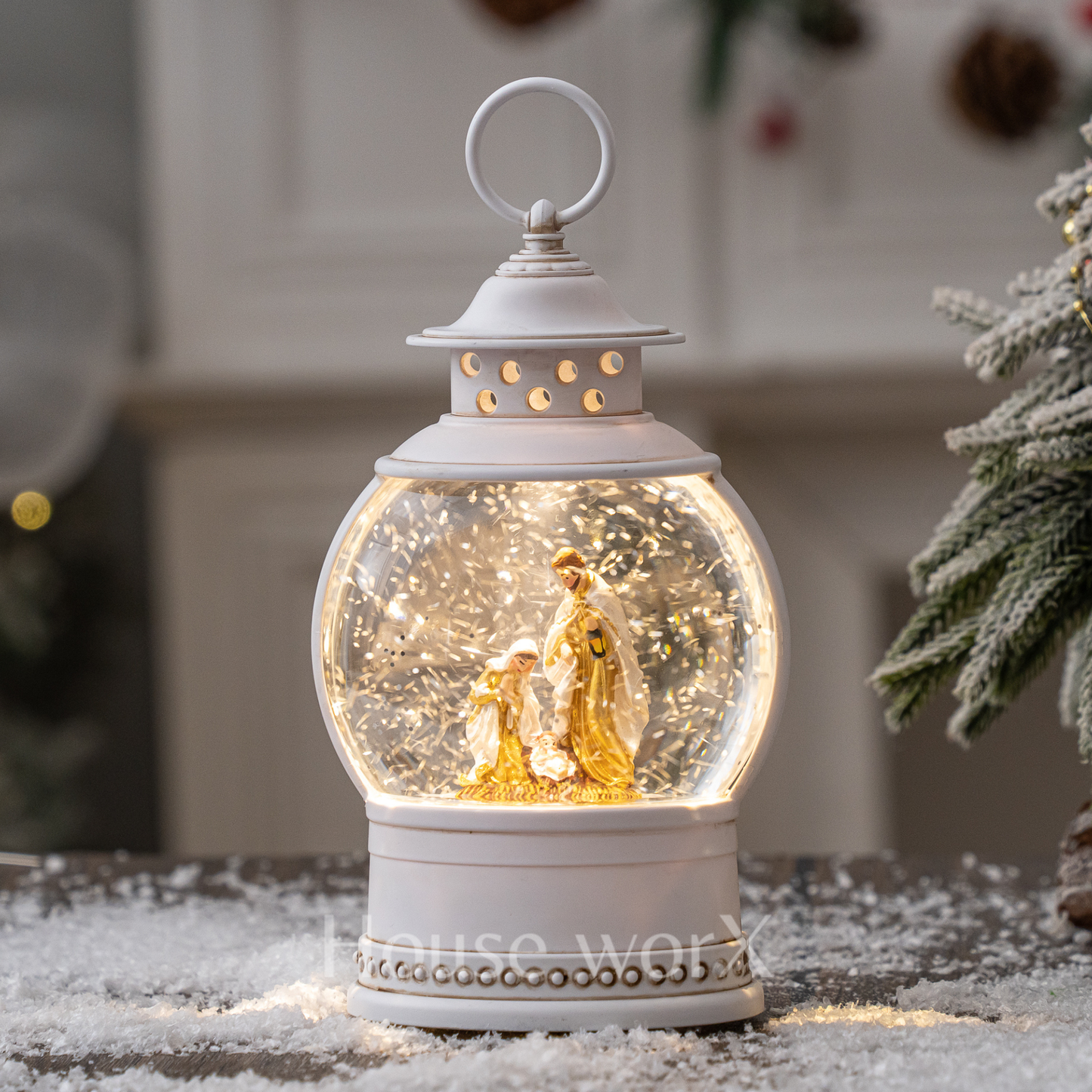 Decorative snow globe with a white lantern base featuring a family scene, placed on a snowy surface.