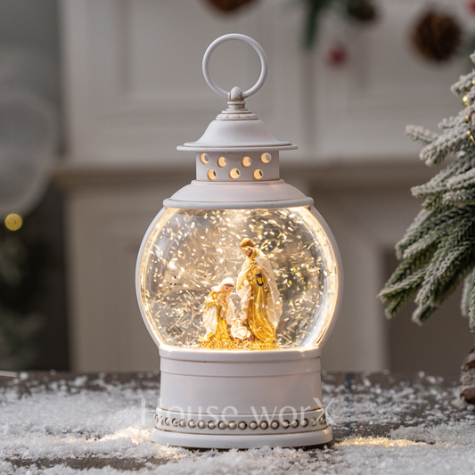 Decorative snow globe with a white lantern base featuring a family scene, placed on a snowy surface.