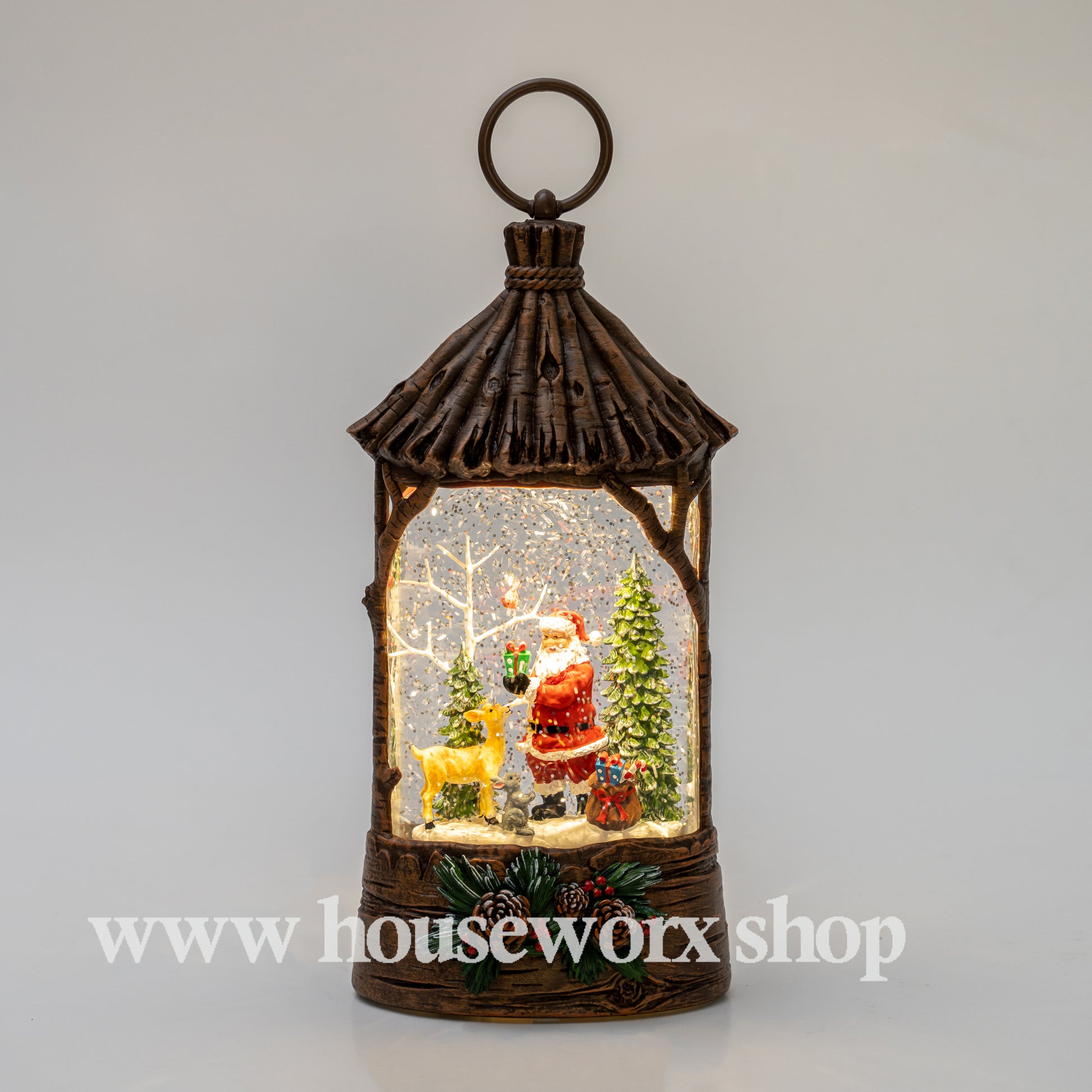Decorative lantern with Santa Claus and Christmas trees inside, on a light gray background. Straw hut christmas snow globe