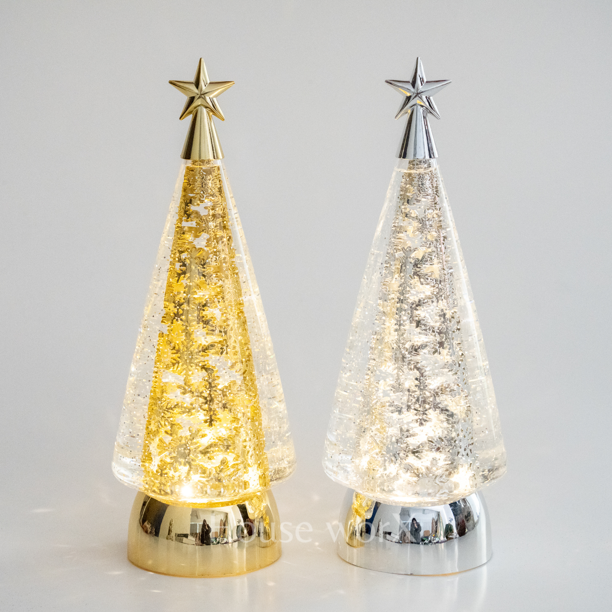 Two decorative Christmas trees with star toppers, one gold and one silver, on a light gray background.