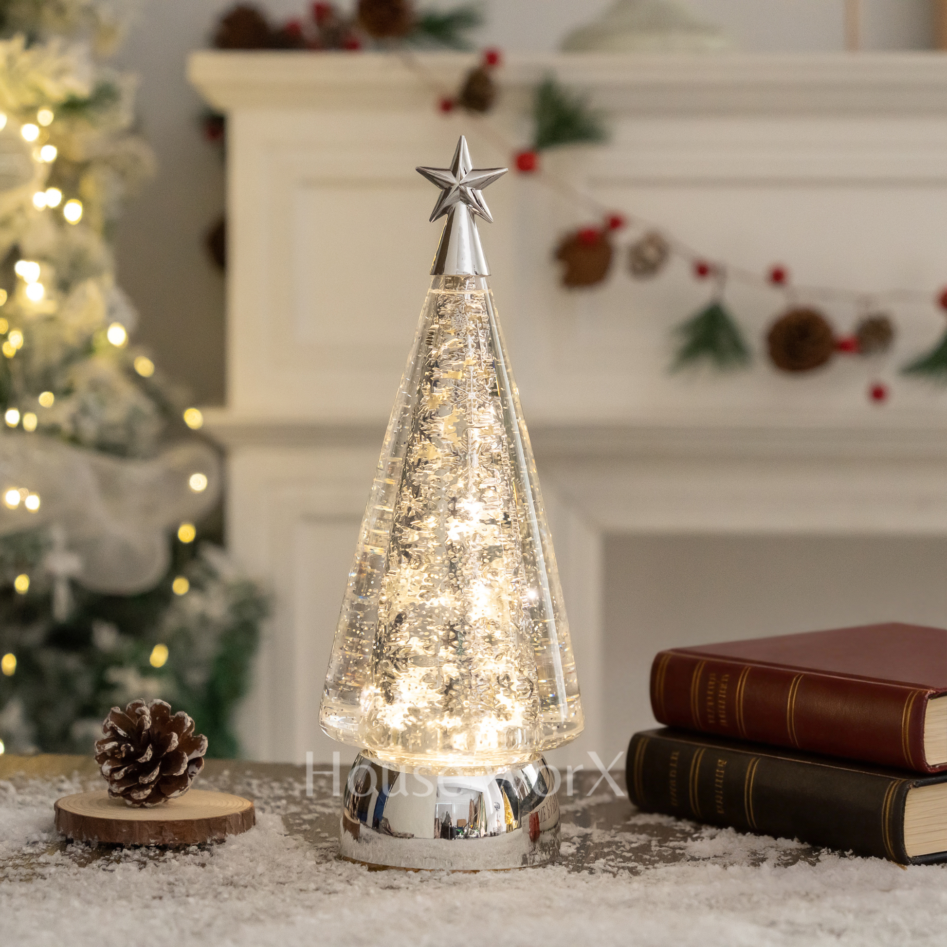 Decorative Christmas tree lamp with a star on top, placed on a surface with books and a pine cone. snow globe