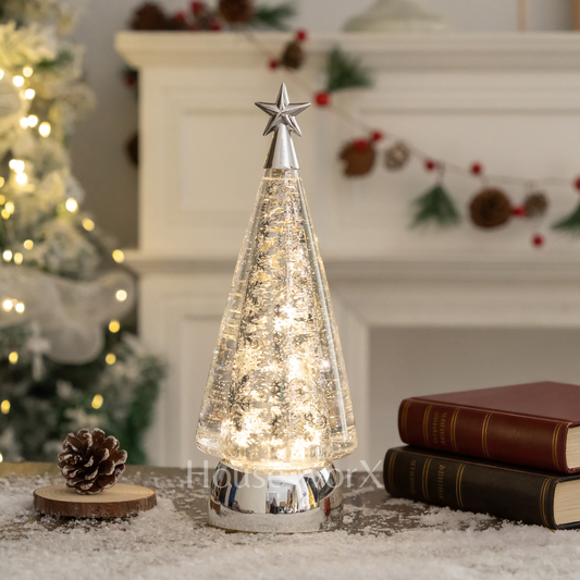 Decorative Christmas tree lamp with a star on top, placed on a surface with books and a pine cone. snow globe